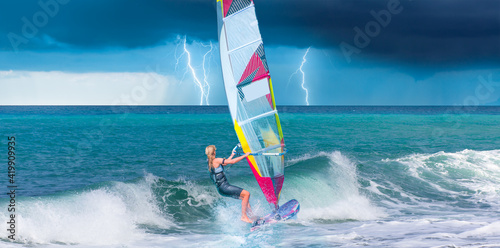 Billede på lærred Windsurfer surfing the wind on waves, strom and lightning in the background  - A