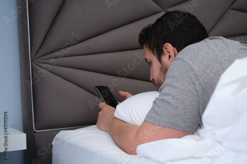 Young latin man with his smartphone in bed late in the morning. Late in bed concept.
