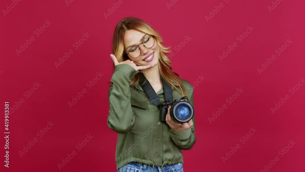 Young blonde girl photographer making phone gesture and speaking with someone. Call me back sign over isolated background Young blonde girl photographer making phone gesture and speaking with someone. Call me back sign over isolated background