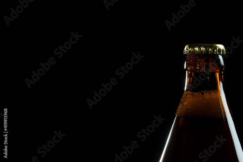 Close-up of a brown beer bottle with a metal lid on a black background with a large space
