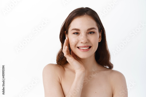 Skin care beauty. Feminine model with hydrated healthy skin, glowing face, touching cheek and smiling with pleased expression, nourish and clean skin with cosmetics, spa concept