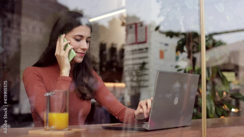 Beautiful business woman speaking mobile phone and working on laptop sitting in cafe.Smiling lady talking smartphone with colleagues or business partners.Closeup portrait beautiful female freelancer Beautiful business woman speaking mobile phone and working on laptop sitting in cafe.Smiling lady talking smartphone with colleagues or business partners.Closeup portrait beautiful female freelancer