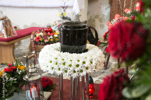 Black urn on the funeral day in church; surrounded with daisies and roses