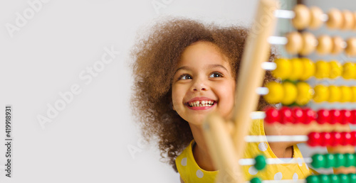 banner of A Black student in a yellow dress laughs brightly behind a colored abacus in an elementary school photo