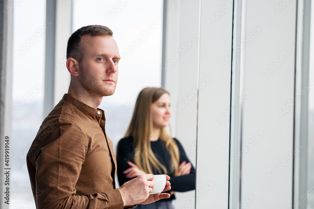 Stylish young couple in love in front of large panoramic windows. A young woman and a man are standing at a large window with coffee. Selective focus Stylish young couple in love in front of large panoramic windows. A young woman and a man are standing at a large window with coffee. Selective focus