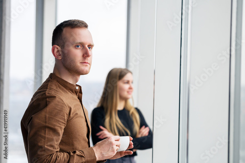 Stylish young couple in love in front of large panoramic windows. A young woman and a man are standing at a large window with coffee. Selective focus