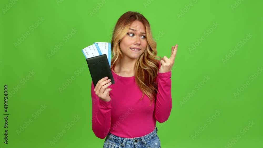 Young blonde girl holding a passport with with fingers crossing over isolated background on green screen chroma key Young blonde girl holding a passport with with fingers crossing over isolated background on green screen chroma key