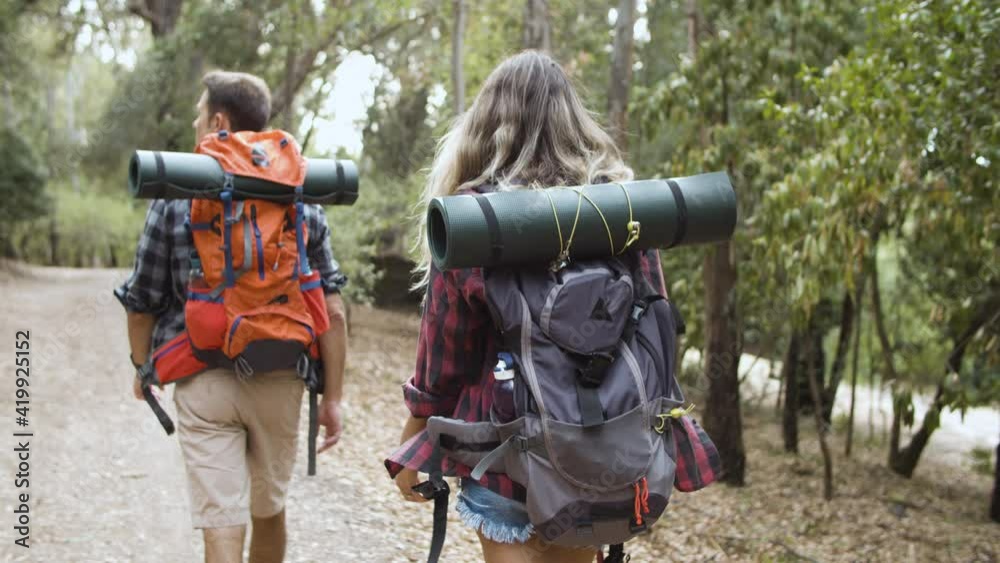 Couple of hikers carrying camping backpacks, walking on forest path, enjoying outdoor vacation and healthy recreation. Dolly shot, back view. Adventure travel concept Couple of hikers carrying camping backpacks, walking on forest path, enjoying outdoor vacation and healthy recreation. Dolly shot, back view. Adventure travel concept