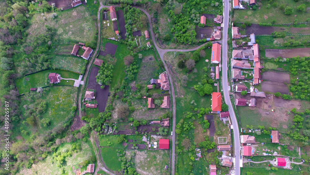 Fototapeta premium Aerial top view of a countryside village in Romania. Rural countryside landscape were the hamlet is located on a hilly region populated by trees.