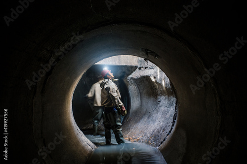 Sewer tunnel worker examines sewer system damage and wastewater leakage