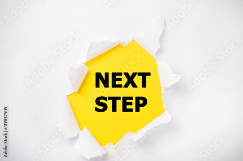 In the center of the torn white sheet on a yellow background is the inscription next step.