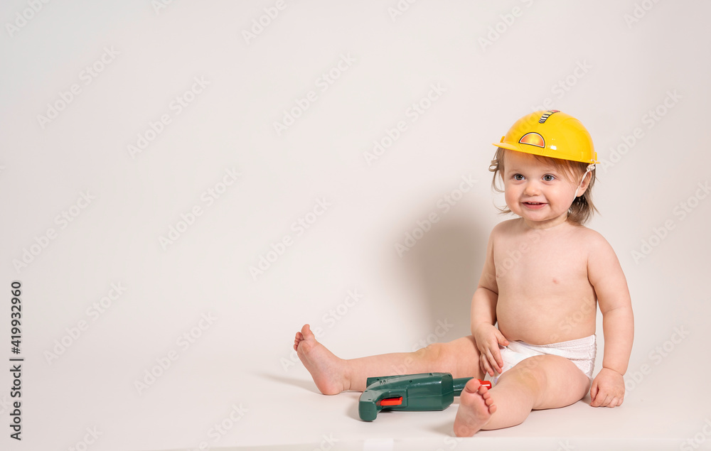 pretty toddler boy, sitting in a diaper and a yellow helmet, with a screwdriver toy lying between his legs pretty toddler boy, sitting in a diaper and a yellow helmet, with a screwdriver toy lying between his legs