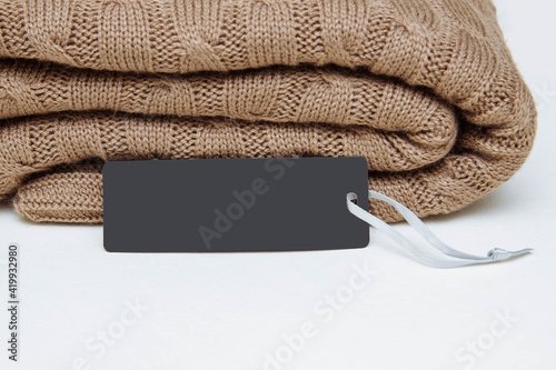 Brown knitted blanket lies folded on a white table with a black paper label close-up, copy space, fabric and clothing care concept, dry cleaning, natural woven wool, eco friendly