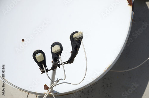 White satellite dish with three converters mounted on residental building rooftop concrete wall. Satellite television photo