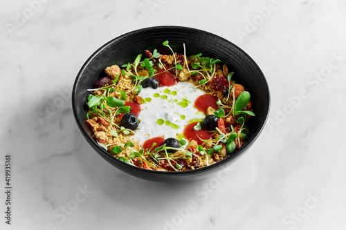 Healthy breakfast bowl of granola with dried fruits, berries, nuts, microgrin and yogurt on a light marble background
