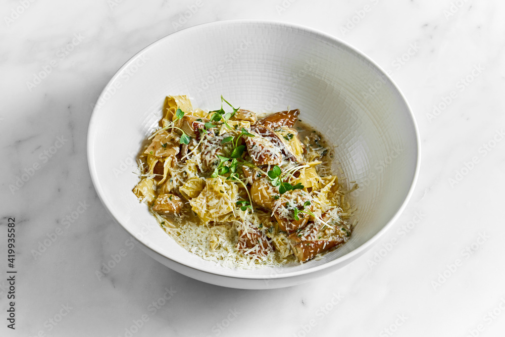 Pappardelle pasta with white forest mushrooms, mushroom sauce, grated parmesan and microgrine in a white bowl on a white marble background
