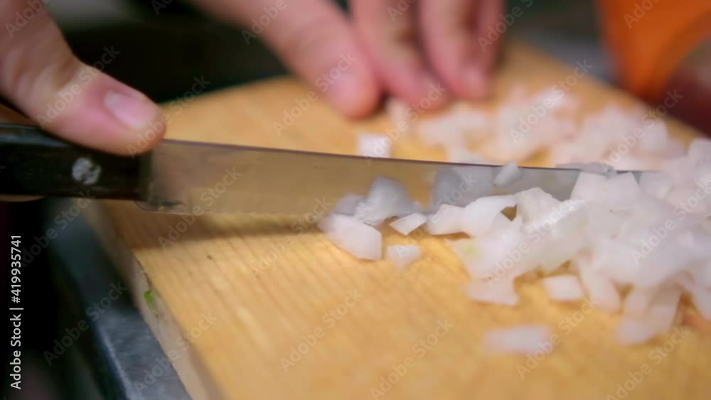 Hands slowly chopping an onion on wooden cutting board Hands slowly chopping an onion on wooden cutting board