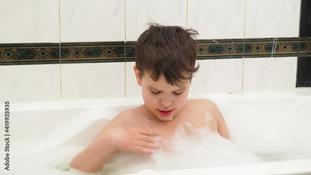 Child playing with foam bubbles while taking a bubble bath. Boy playing with foam while bathing. Cheerful boy having fun with foam indoor. Facial expression. Montessori concept. Pediatrics background Child playing with foam bubbles while taking a bubble bath. Boy playing with foam while bathing. Cheerful boy having fun with foam indoor. Facial expression. Montessori concept. Pediatrics background