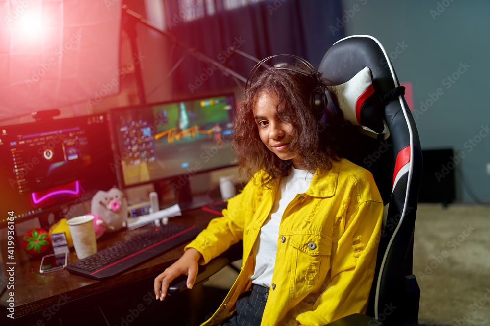 Teenage girl playing video games and sits in hi -tech room with modern computer and big monitors. Closeup. Teenage girl playing video games and sits in hi -tech room with modern computer and big monitors. Closeup.