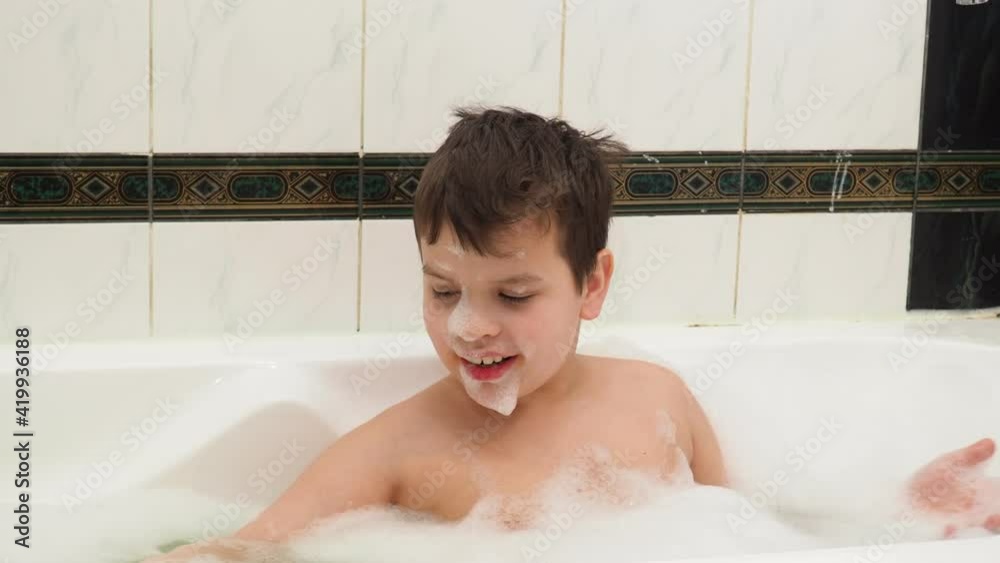 Child playing with foam bubbles while taking a bubble bath. Boy playing with foam while bathing. Cheerful boy having fun with foam indoor. Facial expression. Montessori concept. Pediatrics background Child playing with foam bubbles while taking a bubble bath. Boy playing with foam while bathing. Cheerful boy having fun with foam indoor. Facial expression. Montessori concept. Pediatrics background