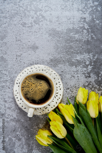 cup of black coffee on stone surface and bouquet of yellow tulips