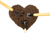Three garden hand tools in a heart shaped pile of soil