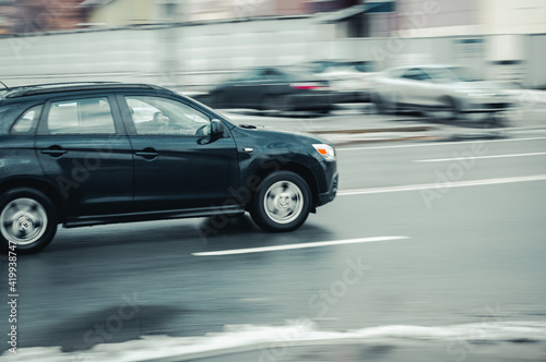fast moving SUV rides on a winter city road. Side view of black car on wet slippery road in motion. Vehicle shot with blurred effect