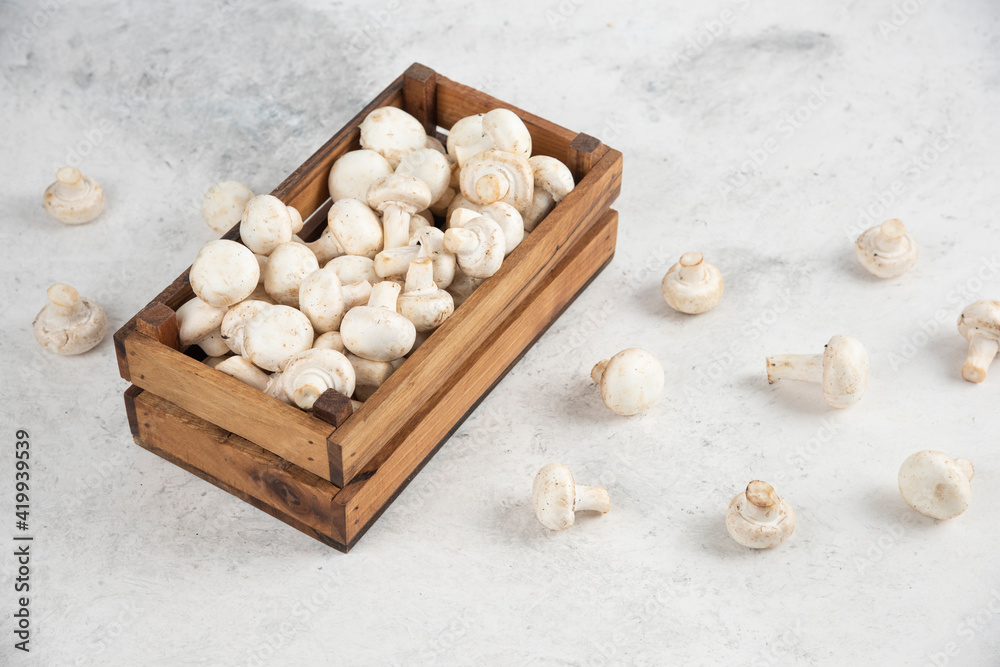 White mushrooms inside a wooden tray on a marble background White mushrooms inside a wooden tray on a marble background
