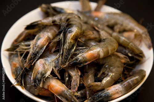 Raw shrimps in a white plate on a black background.