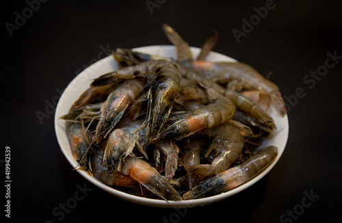 Fototapeta Naklejka Na Ścianę i Meble -  Raw shrimps in a white plate on a black background.