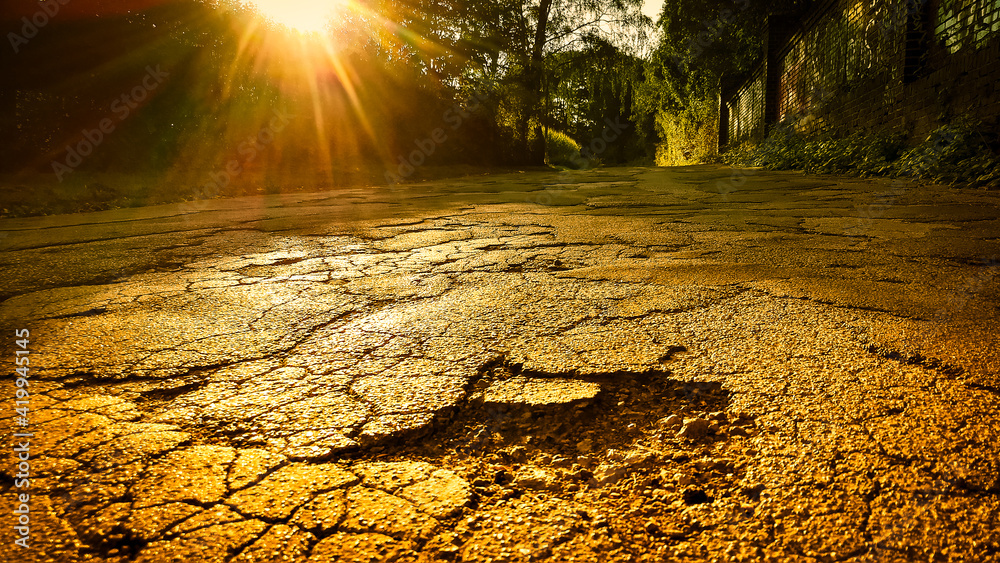cracked road surface with huge pothole in foreground against sunset