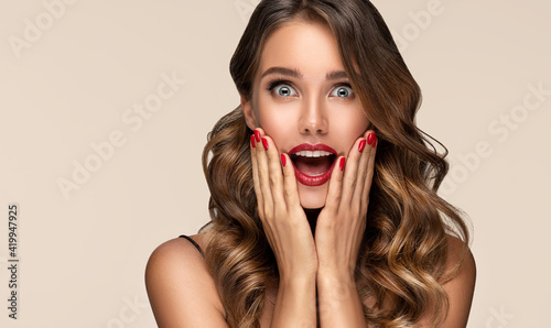 Beautiful shocked and surprised woman screaming .Beauty female with wavy hairstyle. Curly hair girl amazed . Expressive facial expressions . Red nails manicure.Beauty , cosmetic and makeup photo