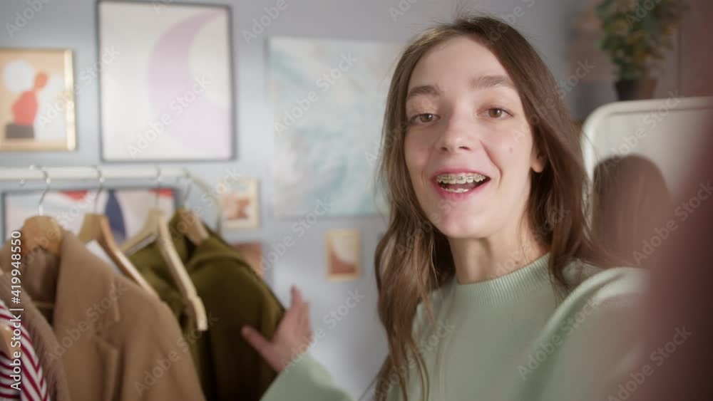 Young beauty blogger recodring selfie, holding clothes looking in camera while taking new fashion video for vlog on phone, blog with, wardrobe consultation, choosing clothes in showroom Young beauty blogger recodring selfie, holding clothes looking in camera while taking new fashion video for vlog on phone, blog with, wardrobe consultation, choosing clothes in showroom