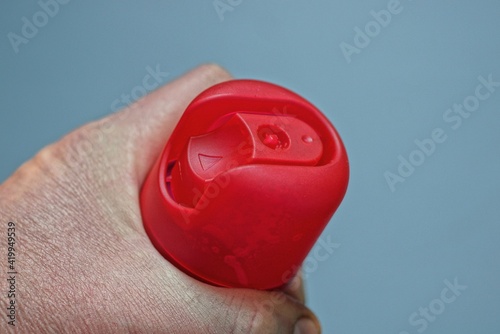 hand holds spray with red cap on gray background