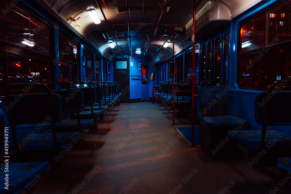 The interior of an empty tram at night . Rows of blue seats on public transit 