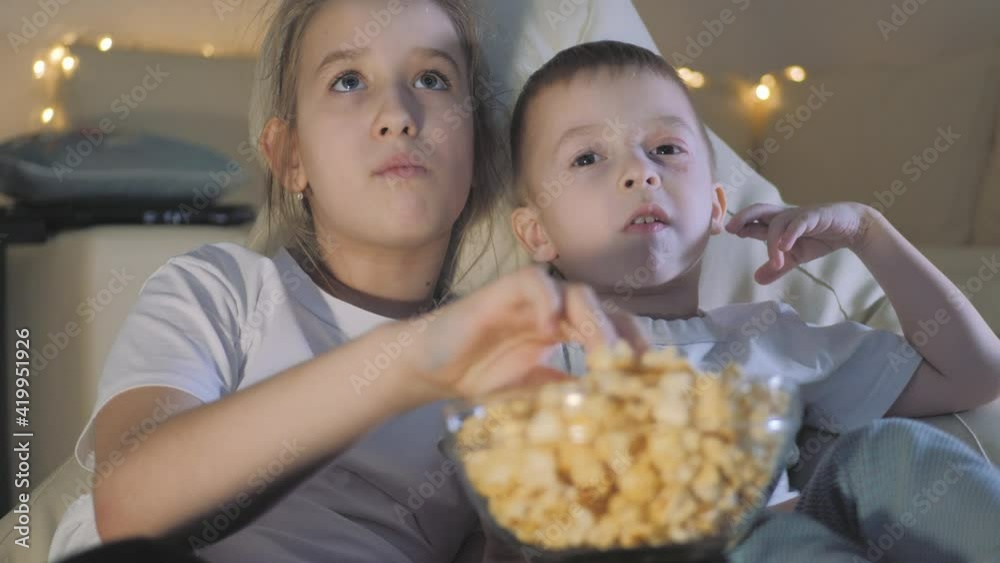 Cute little kids while watching TV. Two children watching TV, eating popcorn sitting on floor at home. Cute child family of two adorable siblings eating popcorn and watching cartoons in living room. Cute little kids while watching TV. Two children watching TV, eating popcorn sitting on floor at home. Cute child family of two adorable siblings eating popcorn and watching cartoons in living room.