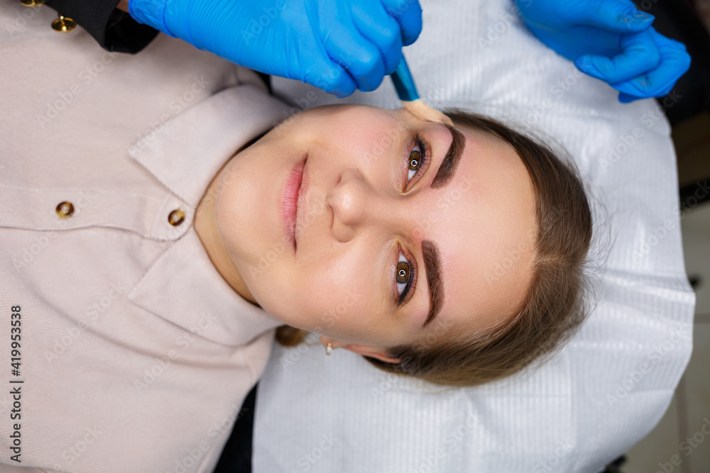 Woman with permanent makeup tattoo on her eyebrows. Close-up beautician makes makeup applies a foundation. Professional make-up and cosmetic skin care. Woman with permanent makeup tattoo on her eyebrows. Close-up beautician makes makeup applies a foundation. Professional make-up and cosmetic skin care.
