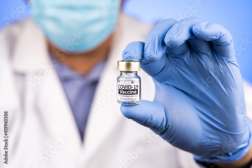 Close-up and focus on Covid-19 vaccine vial held by Asian medical doctor with medical glove in background
