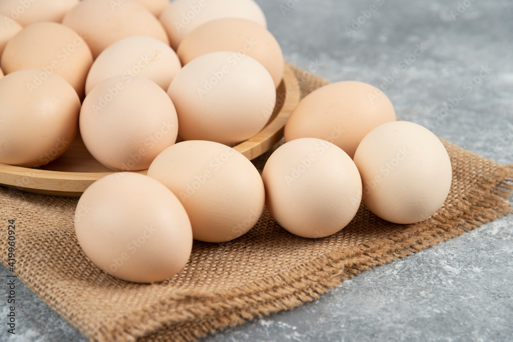 Wooden plate of organic uncooked eggs on marble surface Wooden plate of organic uncooked eggs on marble surface