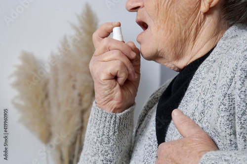 Senior woman spraying breath spray, energy or nitroglycerin spray in her mouth.  photo