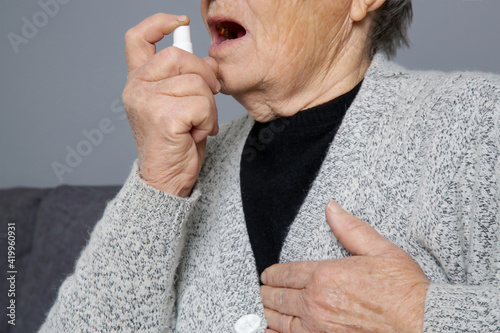 Senior woman spraying breath spray, energy or nitroglycerin spray in her mouth.  photo