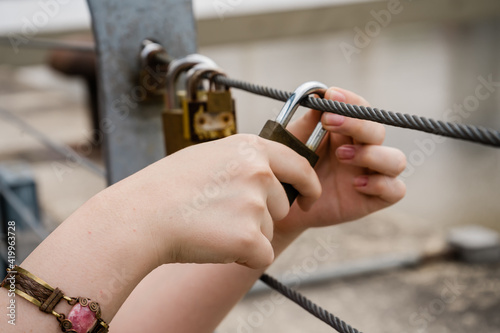 Teenager hands closing a padlock on a bridge.