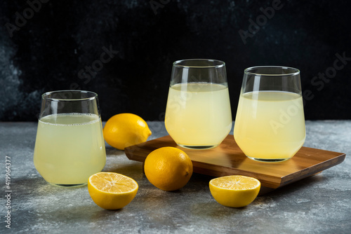 Three glass cups with lemon juice on a wooden board