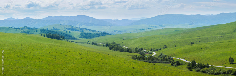 Green meadows and mountain slopes, summer. The road passes through the valley.