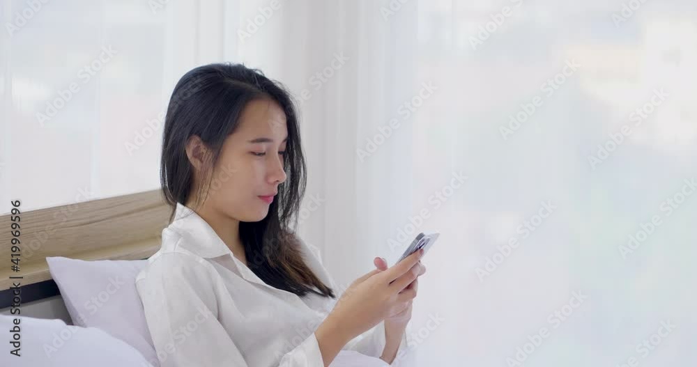 Young blogger Asian woman using smartphone social media to check rating response online page and writing to communicate with fan to keep relation. Relaxing chatting to friend on the bed in white shirt Young blogger Asian woman using smartphone social media to check rating response online page and writing to communicate with fan to keep relation. Relaxing chatting to friend on the bed in white shirt