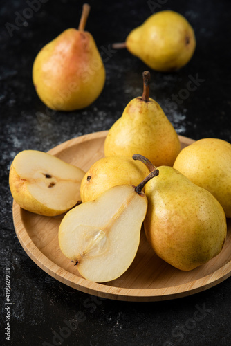Wooden plate of delicious yellow pears on black surface