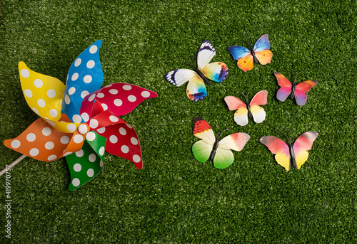 Colorful pinwheel and little colorful butterflies on green grass background. Spring decoration