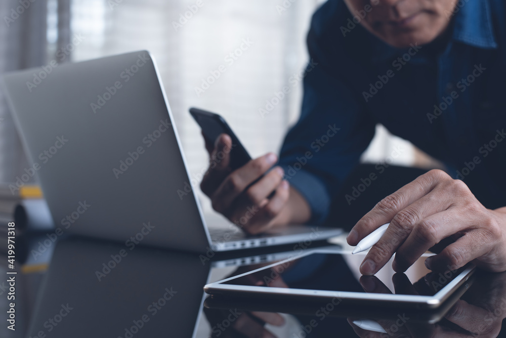 Multitasking business man busy working on digital tablet ,laptop computer and using smartphone at office
