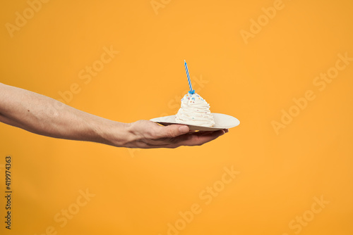 Cake with a candle in a man's hand on a yellow background cropped view Copy Space