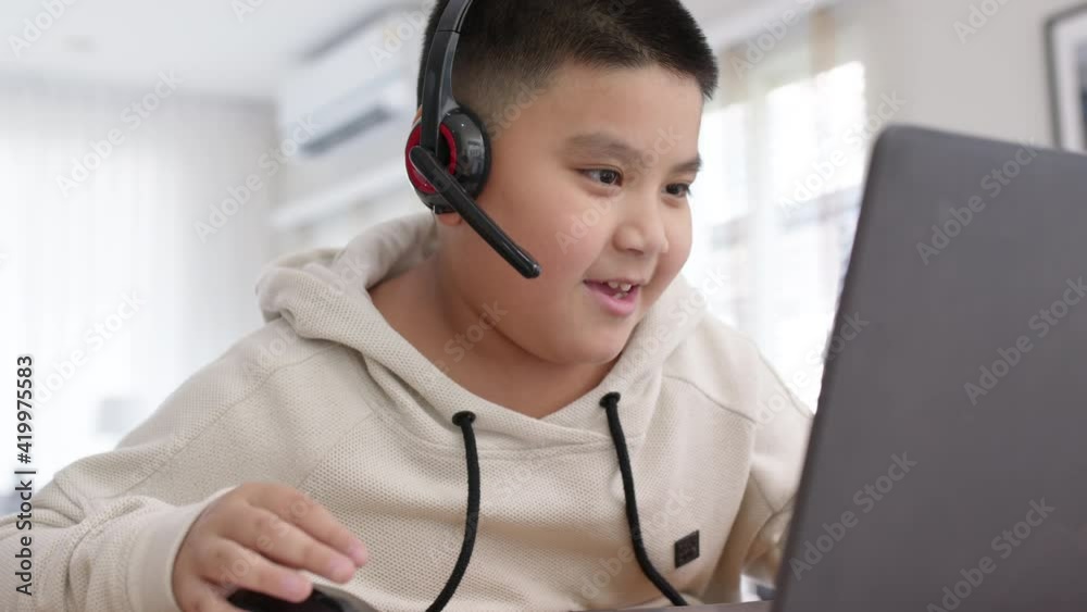 Young asia boy student wear headset headphone with computer laptop videocall talk present online e-learning class study with teacher, social distance learn language at home, homeschooling concept.